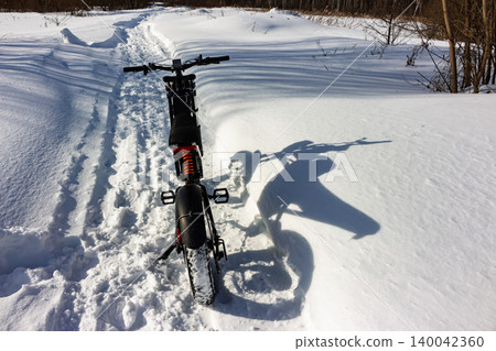 Rugged electric fatbike on a pristine snow trail, its long shadow hinting at winter adventures. Sunny frosty day, extreme e-biking journey Rugged electric fatbike on a pristine snow trail, its long shadow hinting at winter adventures. Sunny frosty day, extreme e-biking journey 140042360