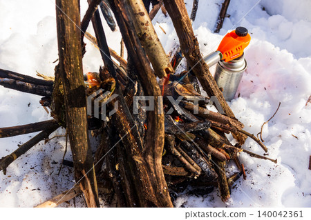 Vibrant orange gas torch quickly ignites kindling for a cozy winter campfire, radiating warmth in snowy wilderness Vibrant orange gas torch quickly ignites kindling for a cozy winter campfire, radiating warmth in snowy wilderness 140042361
