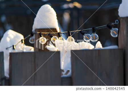Winter park fence adorned with dormant string lights under fresh snow, basking in daylight. Seasonal beauty and serenity Winter park fence adorned with dormant string lights under fresh snow, basking in daylight. Seasonal beauty and serenity 140042545