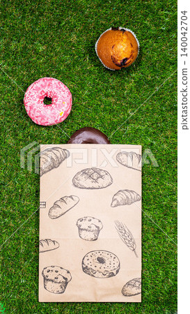 Freshly baked donuts and crumpled paper bag on a grass background .Top view. 140042704