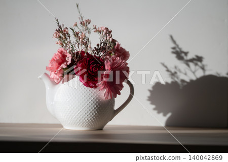 Pink bouquet in a teapot on wooden table white background harsh light Pink bouquet in a teapot on wooden table white background harsh light 140042869