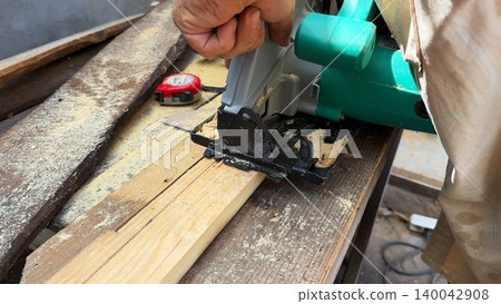 Arms of professional repairman sawing wooden construction with a circular saw at construction. Male hands of adult craftsman cuts wood using electric grind wheel at the site. Slow motion Arms of professional repairman sawing wooden construction with a circular saw at construction. Male hands of adult craftsman cuts wood using electric grind wheel at the site. Slow motion 140042908