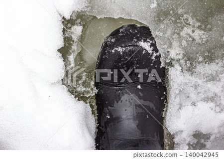 Heavy boot sinking into treacherous, melting river ice. A stark warning of thin ice danger in late winter and fragile surfaces Heavy boot sinking into treacherous, melting river ice. A stark warning of thin ice danger in late winter and fragile surfaces 140042945