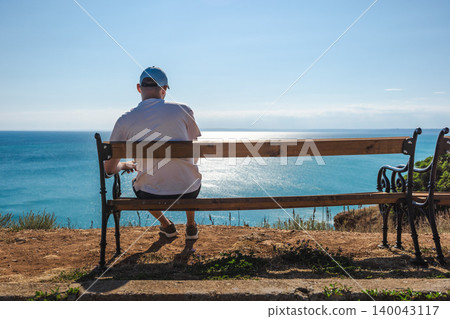Man sitting on bench overlooking Black Sea coastline under sunny blue sky in Bulgaria Man sitting on bench overlooking Black Sea coastline under sunny blue sky in Bulgaria 140043117