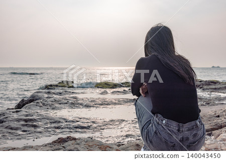 The back view of a woman quietly gazing at the sea from a rocky beach. The back view of a woman quietly gazing at the sea from a rocky beach. 140043450