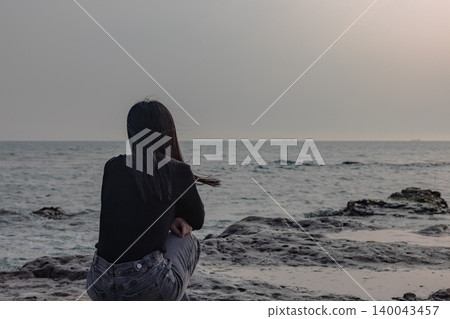 The back view of a woman quietly gazing at the sea from a rocky beach. The back view of a woman quietly gazing at the sea from a rocky beach. 140043457