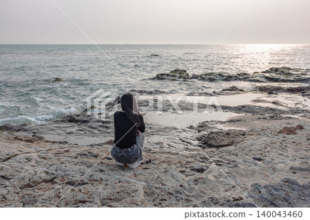 The back view of a woman quietly gazing at the sea from a rocky beach. The back view of a woman quietly gazing at the sea from a rocky beach. 140043460
