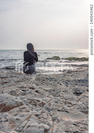 The back view of a woman quietly gazing at the sea from a rocky beach. The back view of a woman quietly gazing at the sea from a rocky beach. 140043462