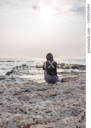 一位女子背對著鏡頭,靜靜地站在岩石沙灘上凝望大海。 一位女子背對著鏡頭,靜靜地站在岩石沙灘上凝望大海。 140043464