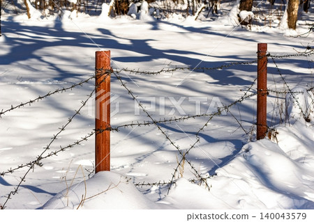 Rusty barbed wire border restricts access across a stark, snowy winter landscape under bright sun Rusty barbed wire border restricts access across a stark, snowy winter landscape under bright sun 140043579