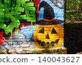 Vibrant street art features a spooky jack-o'-lantern face with a witch hat painted on a weathered brick wall next to wild green graffiti: 140043627