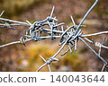 Close-up of weathered, tangled barbed wire forms a stark barrier. Sharp spikes create a sense of danger, restriction, and security around a forbidden zone 140043644