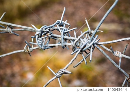 Close-up of weathered, tangled barbed wire forms a stark barrier. Sharp spikes create a sense of danger, restriction, and security around a forbidden zone 140043644