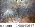 Shimmering ice patterns over a frozen puddle. Nature's abstract winter art, reflecting bare branches and trapped bubbles 140043647
