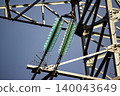 Bright turquoise glass insulators on a robust steel power tower against a vivid blue sky. Crucial elements of high-voltage transmission lines, symbolizing energy and progress 140043649