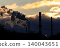 Towering industrial smokestacks spew dark plumes against a vivid sunset sky, highlighting energy production and environmental impact 140043651