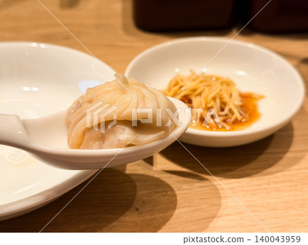 A xiao long bao on a spoon. A plate of ginger and black vinegar to eat with the xiao long bao. A xiao long bao on a spoon. A plate of ginger and black vinegar to eat with the xiao long bao. 140043959