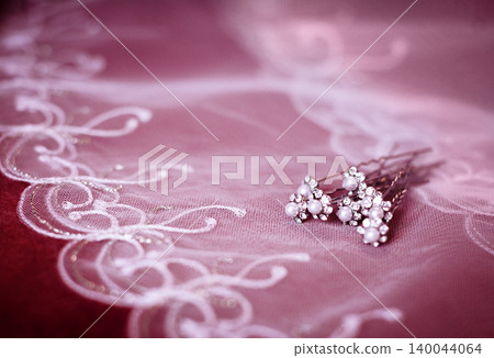 Pearl and crystal bridal hair pins on embroidered lace fabric, soft pink background Pearl and crystal bridal hair pins on embroidered lace fabric, soft pink background 140044064