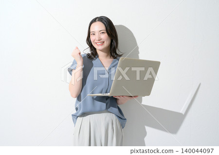 A Japanese woman makes a triumphant gesture while holding a laptop against a white background. A Japanese woman makes a triumphant gesture while holding a laptop against a white background. 140044097