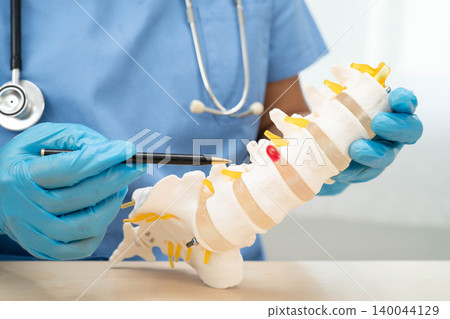 Asian doctor holding spinal nerve and bone model, Lumbar spine displaced herniated disc fragment for treatment medical in the orthopedic department. Asian doctor holding spinal nerve and bone model, Lumbar spine displaced herniated disc fragment for treatment medical in the orthopedic department. 140044129