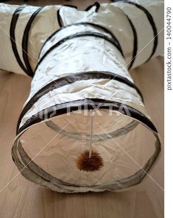 A white, collapsible, crinkly tunnel with three entrances and a dangling fur pom-pom. A white, collapsible, crinkly tunnel with three entrances and a dangling fur pom-pom. 140044790