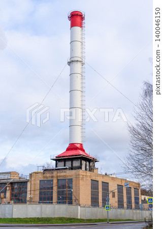 Towering white chimney extends upward from brick boilerhouse showing industrial design elements 140046150