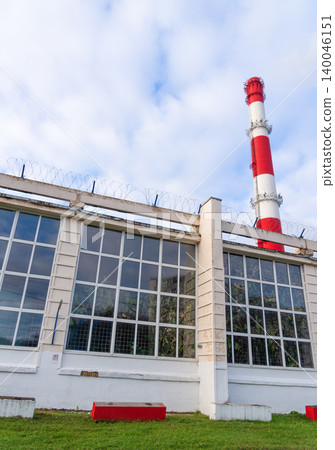 Bright sky enhances sleek factory appearance. Factory windows display chimney shadows and grassy ground 140046151