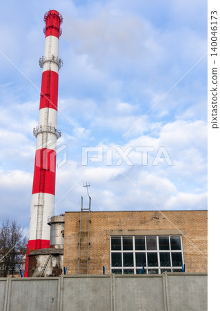 Red and white chimney against cloudy sky. Vertical view of factory chimney with brick facade Red and white chimney against cloudy sky. Vertical view of factory chimney with brick facade 140046173