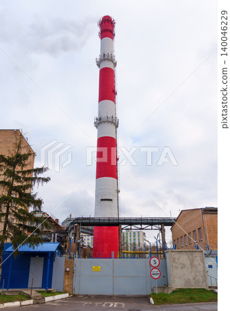 Factory with chimney. An expansive industrial landscape featuring prominent striped smokestack and gates Factory with chimney. An expansive industrial landscape featuring prominent striped smokestack and gates 140046229