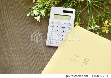 一個標有“工資”字樣的棕色信封和一個計算器 一個標有“工資”字樣的棕色信封和一個計算器 140047251