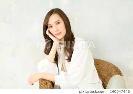 A woman sitting in a chair, resting her chin on her hand. A woman sitting in a chair, resting her chin on her hand. 140047446