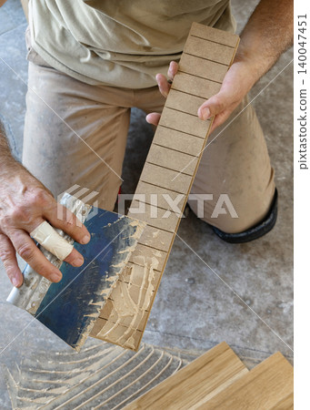 Construction worker applying adhesive on parquet planks during flooring installation in apartment Construction worker applying adhesive on parquet planks during flooring installation in apartment 140047451