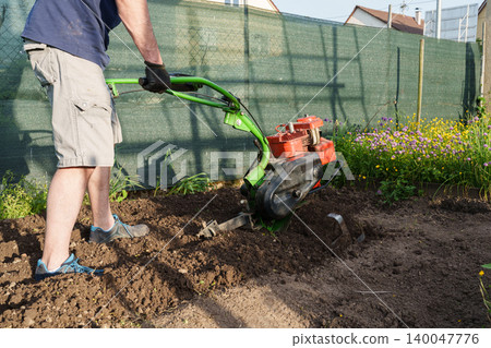 Man using motor cultivator to prepare soil in garden Man using motor cultivator to prepare soil in garden 140047776
