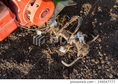 Rotary tiller blades cultivating soil close up Rotary tiller blades cultivating soil close up 140047777