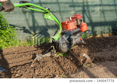 Man using motor cultivator to prepare soil in garden 140047778