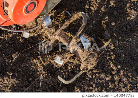Rotary tiller blades cultivating soil close up Rotary tiller blades cultivating soil close up 140047782