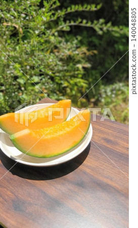 Fresh, juicy red-fleshed cut melons arranged on a white plate, photographed outdoors amidst the beautiful fresh greenery. Fresh, juicy red-fleshed cut melons arranged on a white plate, photographed outdoors amidst the beautiful fresh greenery. 140048805