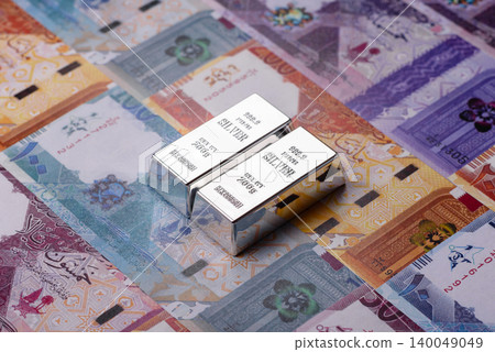A silver bar, white metal against a backdrop of Qatari money, as a concept. A silver bar A silver bar, white metal against a backdrop of Qatari money, as a concept. A silver bar 140049049