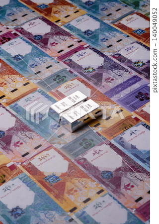 A silver bar, white metal against a backdrop of Qatari money, as a concept. A silver bar A silver bar, white metal against a backdrop of Qatari money, as a concept. A silver bar 140049052