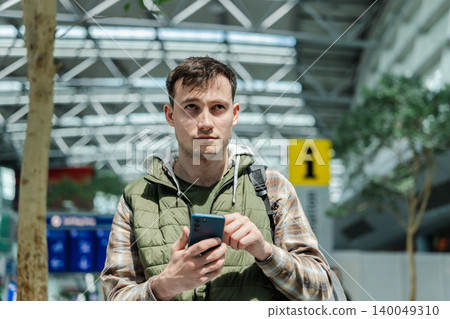 Young male passenger checking smartphone while waiting inside modern airport terminal Young male passenger checking smartphone while waiting inside modern airport terminal 140049310