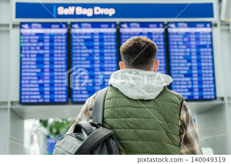 Young traveler looking at airport departure board near self bag drop area Young traveler looking at airport departure board near self bag drop area 140049319