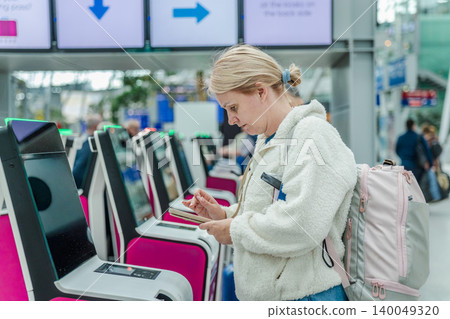 Woman using self check in kiosk with smartphone at modern airport terminal 140049320