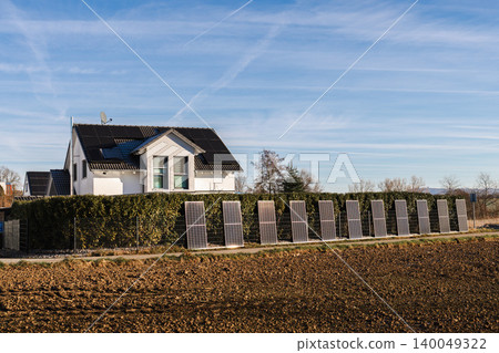 Modern family house with rooftop solar panels and photovoltaic modules near field in rural Germany under blue sky Modern family house with rooftop solar panels and photovoltaic modules near field in rural Germany under blue sky 140049322