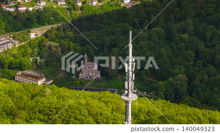 Aerial view of modern communication tower above green forest with historic building and residential area in Germany during sunny spring day Aerial view of modern communication tower above green forest with historic building and residential area in Germany during sunny spring day 140049323