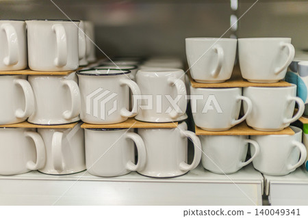 White ceramic mugs arranged on shelf in kitchenware and household goods store 140049341