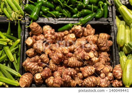 Fresh Jerusalem artichokes with zucchini and green peppers displayed in supermarket produce section, organic root vegetables for healthy cooking Fresh Jerusalem artichokes with zucchini and green peppers displayed in supermarket produce section, organic root vegetables for healthy cooking 140049441