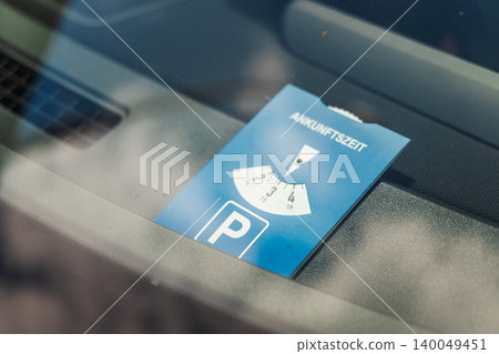 German parking disc with inscription "Ankunftszeit" meaning "arrival time" placed inside car windshield for time limited parking regulation 140049451