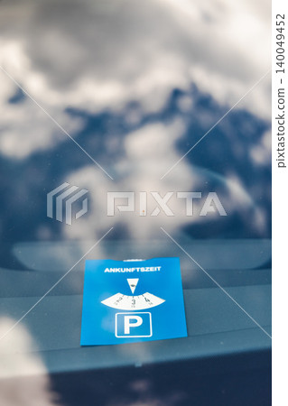 Blue German parking disc with word Ankunftszeit translated as arrival time visible through car windshield in public parking area Blue German parking disc with word Ankunftszeit translated as arrival time visible through car windshield in public parking area 140049452