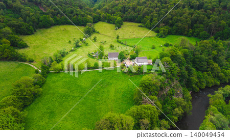 Aerial view of rural farmhouse surrounded by green fields and dense forest near river in western Germany countryside during spring season Aerial view of rural farmhouse surrounded by green fields and dense forest near river in western Germany countryside during spring season 140049454