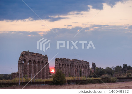 Sunset behind ancient Roman aqueduct in Parco degli Acquedotti Rome with warm light passing through arches and expansive evening sky 140049522